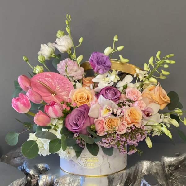 Mixed bouquet with pink tulips, roses, orchids, and anthurium in a white hatbox