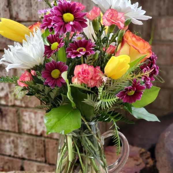 Mixed bouquet of daisies, tulips, and carnations in a clear glass pitcher