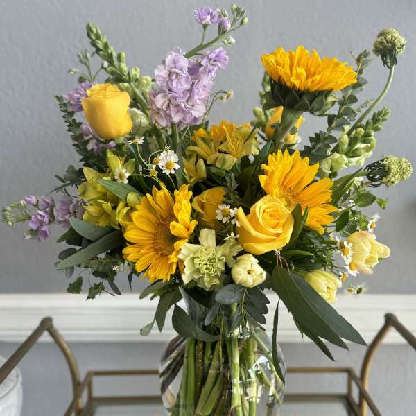 Bouquet of yellow roses, sunflowers, and lavender flowers in a glass vase
