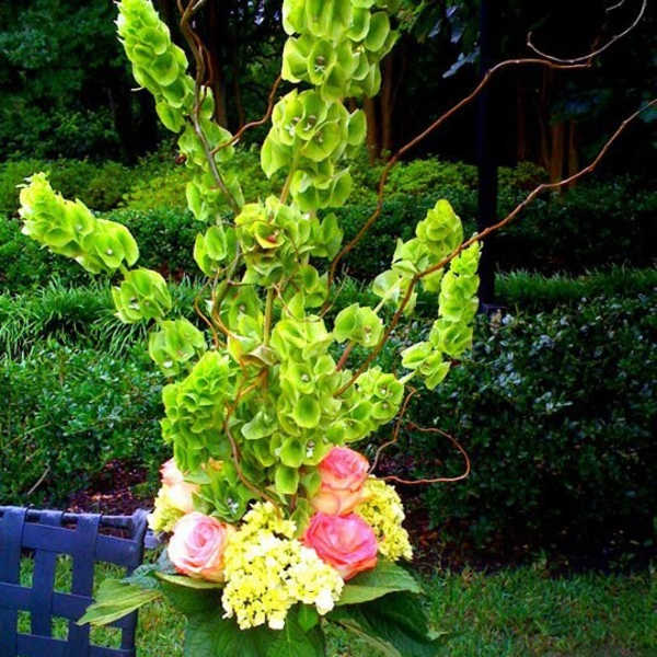 Tall floral arrangement with pink roses and green blooms in a glass vase