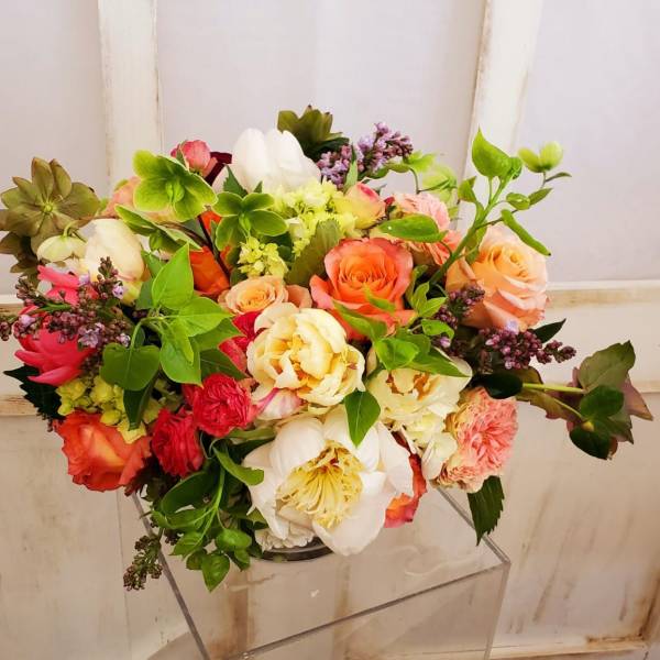 Mixed bouquet of roses, peonies, and other blooms in a clear vase