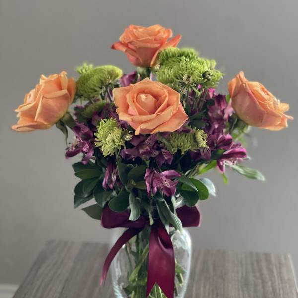 Peach roses and purple flowers in a glass vase with a ribbon