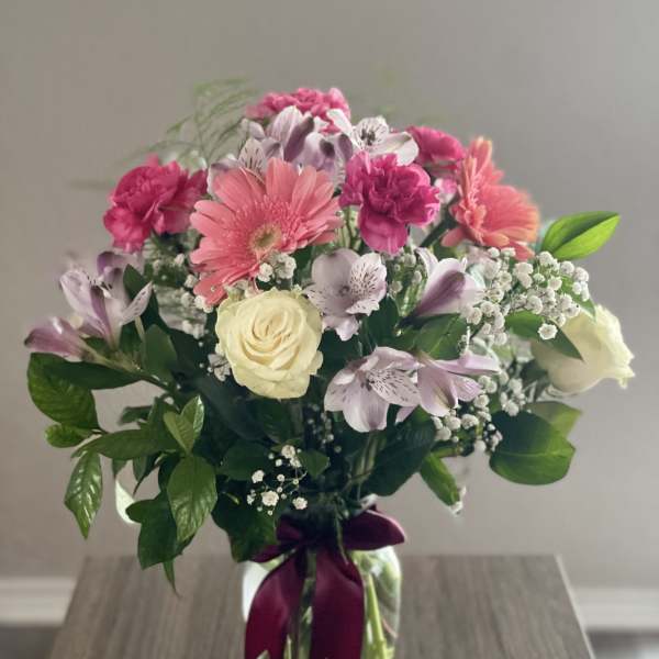 Mixed pink and white bouquet in a glass vase with a purple ribbon