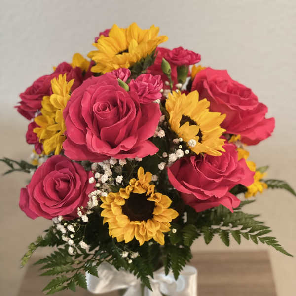 Bouquet of pink roses and yellow sunflowers in a glass vase with a white ribbon