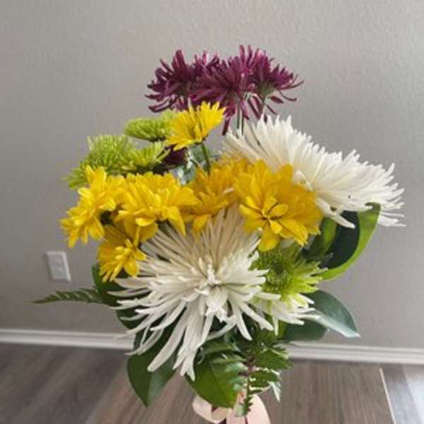 Bouquet of white, yellow, green, and purple chrysanthemum blooms in a pink vase