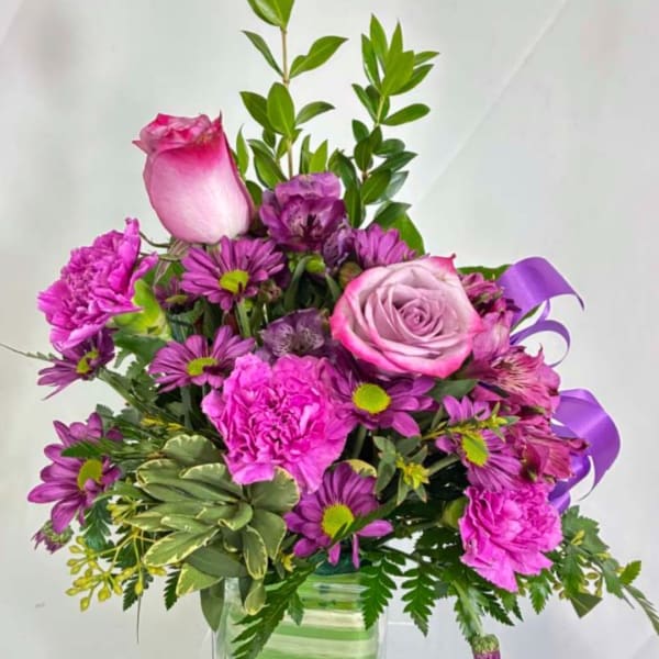 Pink and purple bouquet with roses, carnations, and daisies in a glass vase