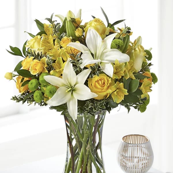 Yellow roses and white lilies arranged in a clear glass vase