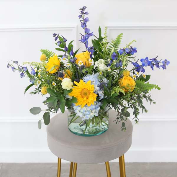 Mixed bouquet in a clear glass vase with yellow, blue, and white flowers