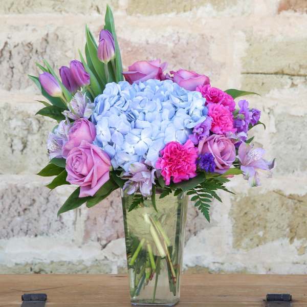 Pink and purple bouquet with blue hydrangea in a clear glass vase