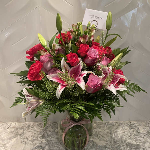 Pink roses and lilies arranged in a glass vase with a ribbon