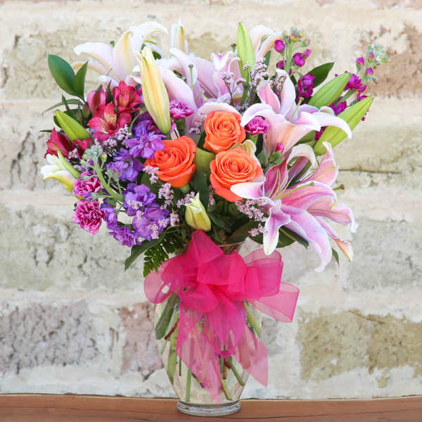 Bouquet of lilies, roses, and purple flowers in a glass vase with a pink ribbon