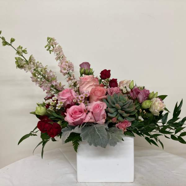Pink and red roses with succulents in a white square vase