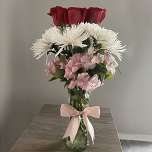 Bouquet of red roses, white spider mums, and pink flowers in a glass vase