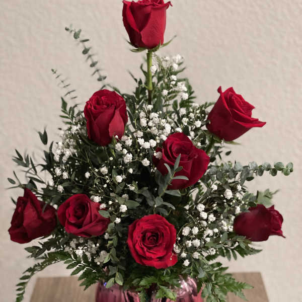 Red roses arranged in a pink glass vase with white filler flowers