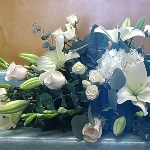 White lilies and roses arranged low with blue accents on a table