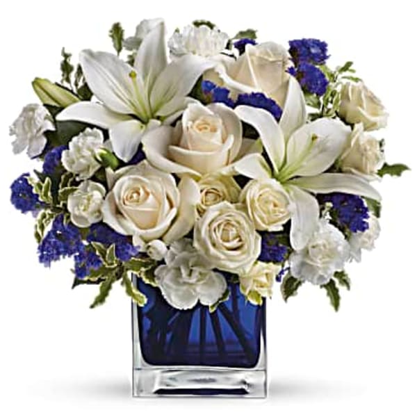 White lilies and roses in a blue glass vase with purple accents