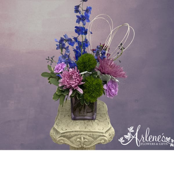Purple and blue floral arrangement in a square glass vase