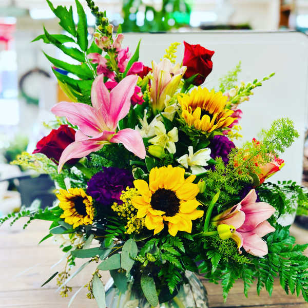 Mixed bouquet with sunflowers, pink lilies, and red roses in a glass vase