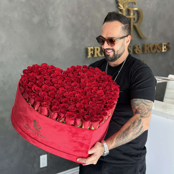 Heart-shaped box of red roses held by a man in sunglasses