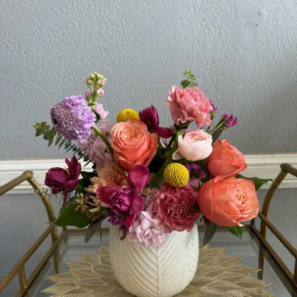 Colorful arrangement of pink, orange, and purple flowers in a white textured vase on a glass cart