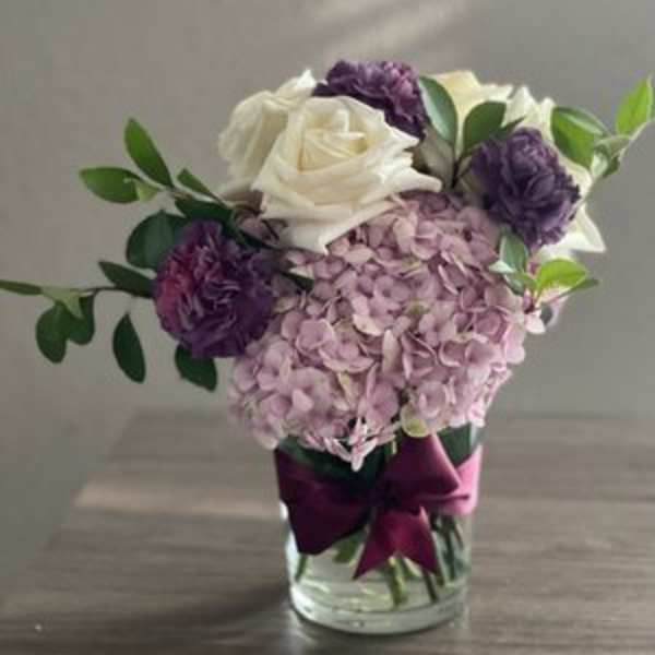 Pink hydrangea and white roses in a glass vase with purple blooms