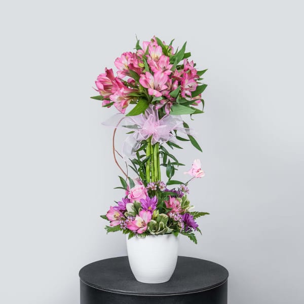 Tall pink flower arrangement in a white vase with a ribbon bow