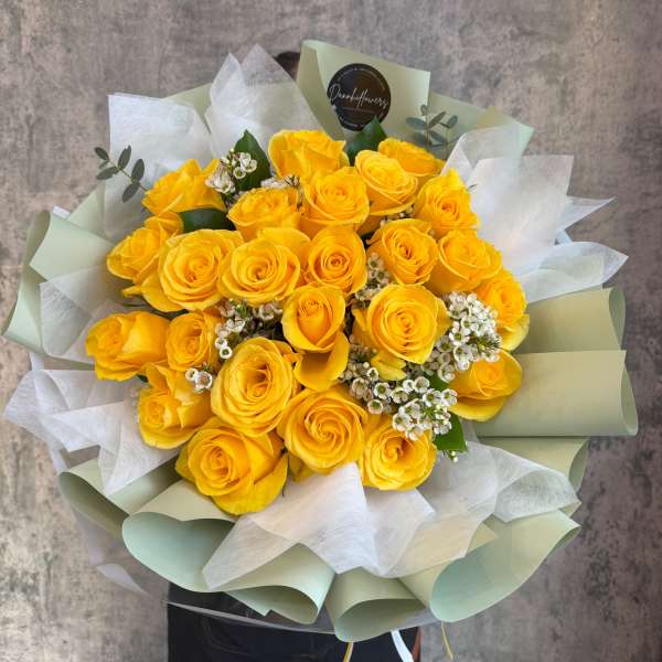 Bouquet of yellow roses with white filler flowers wrapped in pale paper