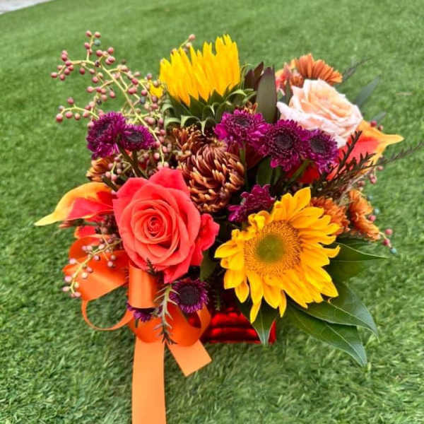 Colorful bouquet with roses, sunflowers, and purple blooms tied with orange ribbon