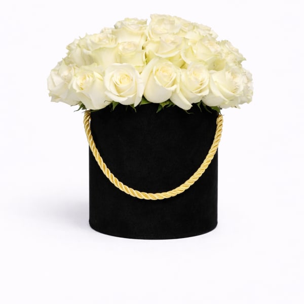 Round box of white roses in a black hatbox with a gold rope handle