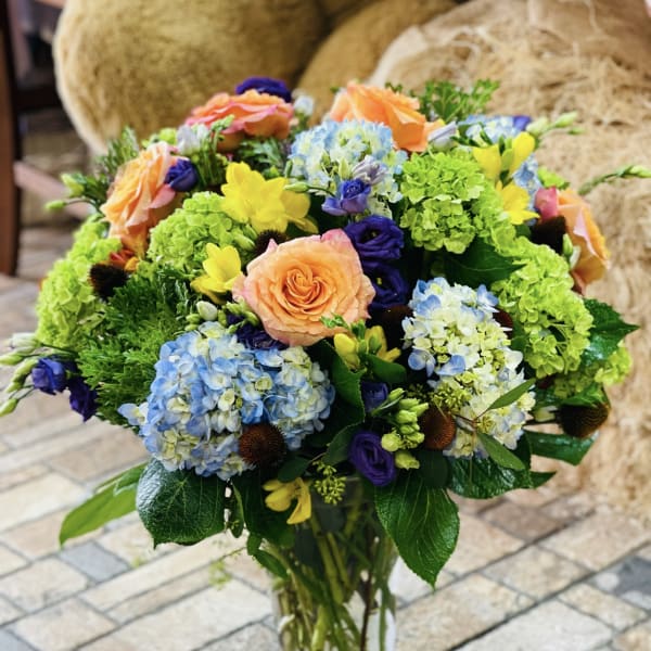 Mixed bouquet in a clear glass vase with peach roses and blue hydrangeas