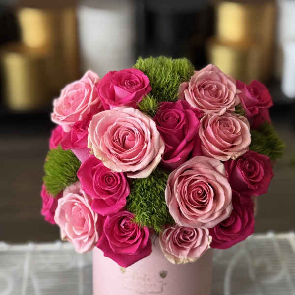 Pink and hot pink roses arranged in a round box with green moss accents