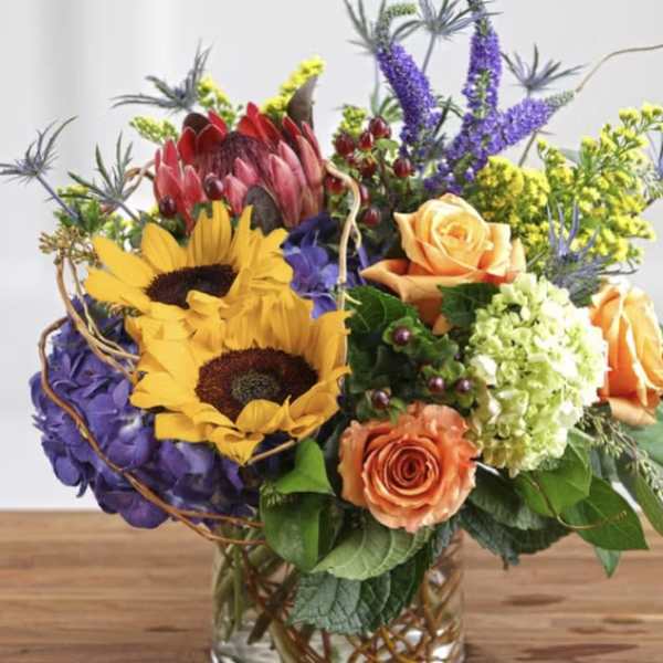 Mixed bouquet with sunflowers, roses, hydrangea, and purple spikes in a glass vase