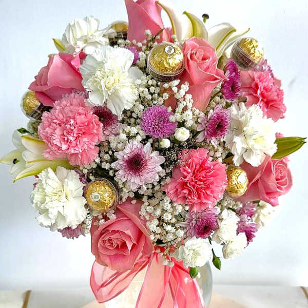 Pink and white bouquet in a glass vase with gold chocolates and a pink ribbon