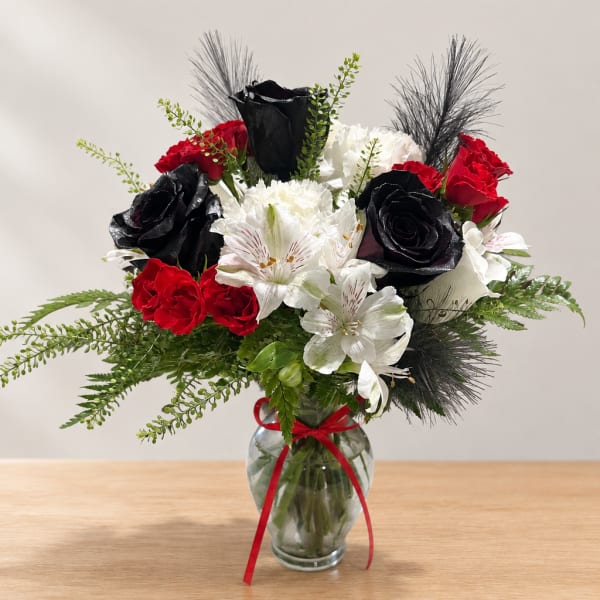 Bouquet of red, white, and black flowers in a glass vase with a red ribbon
