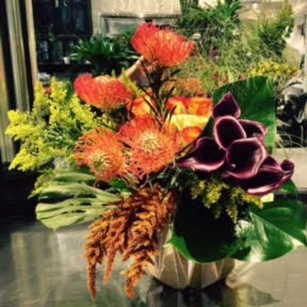 Tropical floral arrangement with orange blooms and purple calla lilies in a vase
