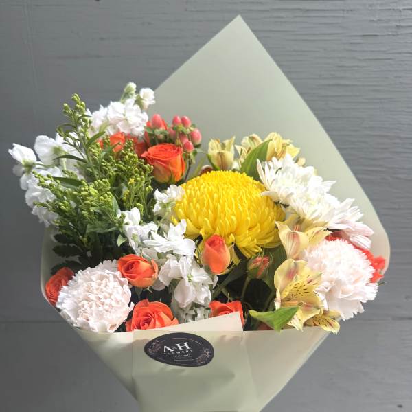 Bouquet of yellow, orange, and white flowers wrapped in pale paper