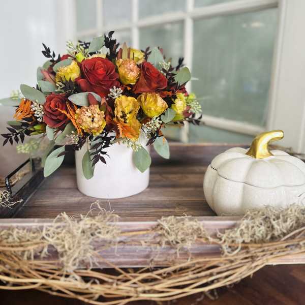 Red and yellow roses in a white vase beside a decorative pumpkin