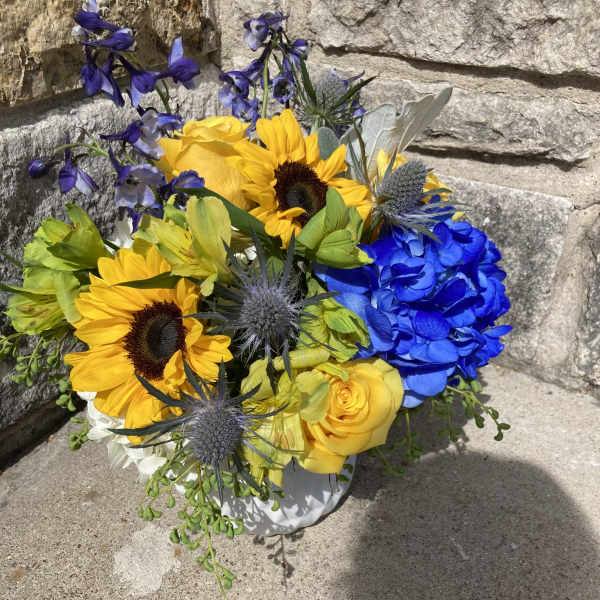 Bouquet with sunflowers, yellow roses, blue hydrangea, and purple flowers in a white vase