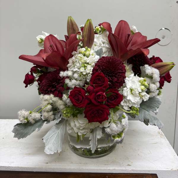 Red lilies and roses arranged in a clear glass vase with white blooms