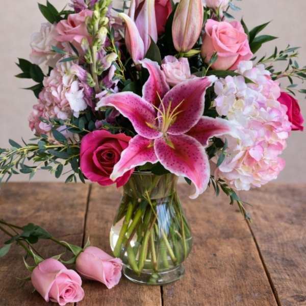 Pink lilies and roses arranged in a clear glass vase