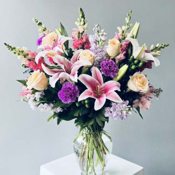Mixed bouquet of pink lilies, roses, and purple flowers in a clear glass vase