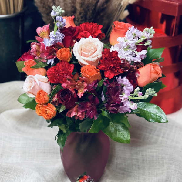 Bouquet of mixed roses and flowers in a purple vase with chocolate-covered strawberries below
