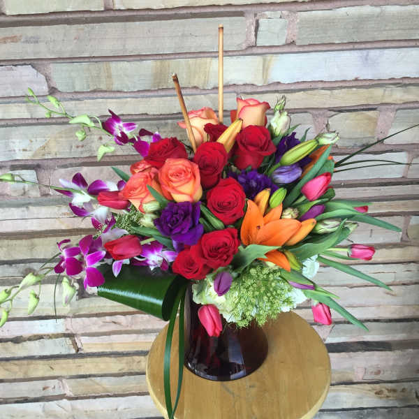 Mixed bouquet of roses, lilies, and orchids in a dark glass vase