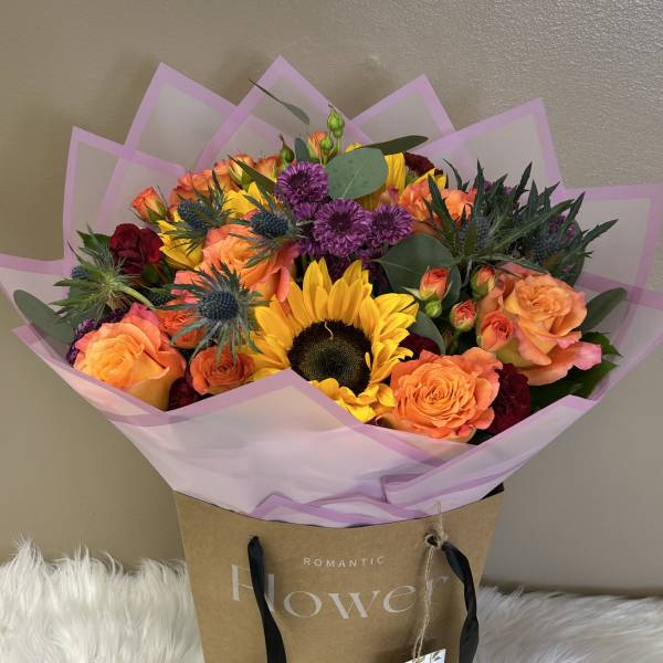 Bouquet of orange roses, sunflowers, and purple blooms in pink wrap