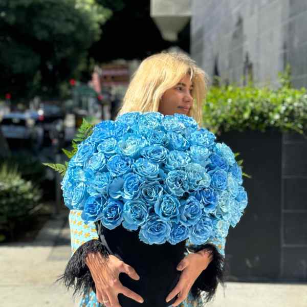 Woman holding a large bouquet of bright blue roses in a black vase
