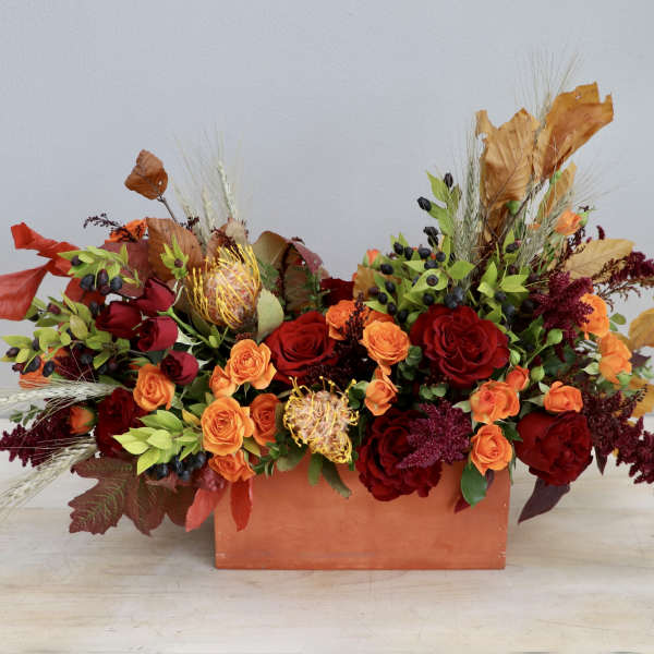 Low rectangular arrangement of red and orange roses with pincushion protea in an orange container