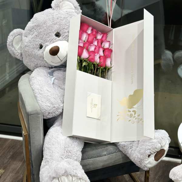 Large teddy bear holding a box of pink roses