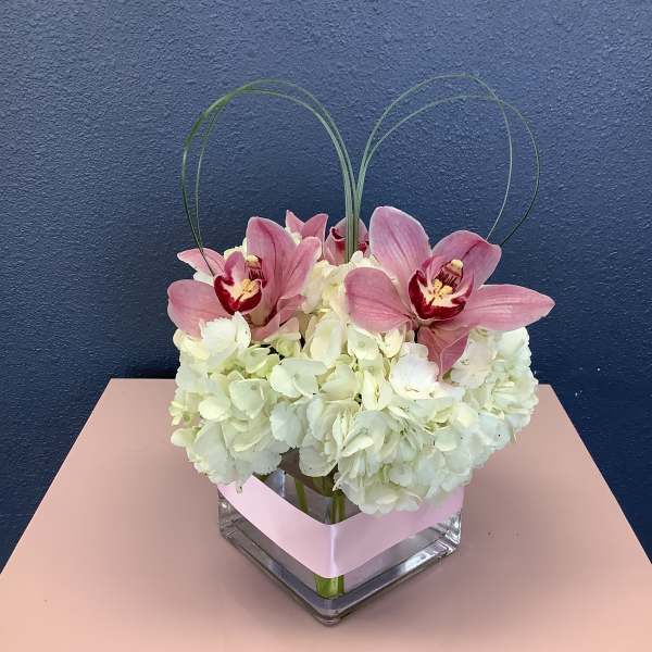 Pink orchids and white hydrangeas in a square glass vase with looped grass