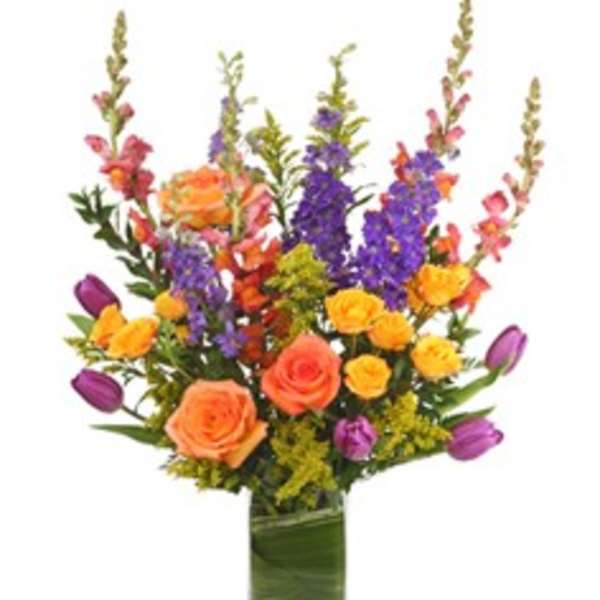 Colorful bouquet of roses, tulips, and purple spikes in a glass vase