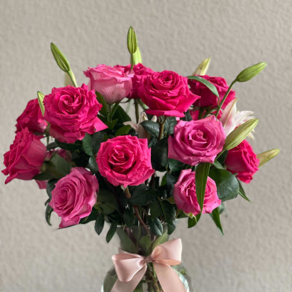 Pink roses and lily buds arranged in a glass vase with a ribbon